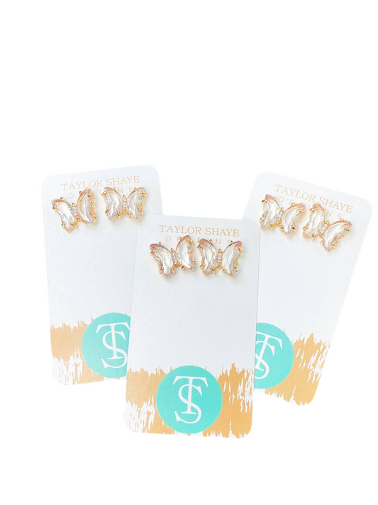 Three pairs of butterfly-shaped stud earrings on a white card with a brand logo, against a white background.