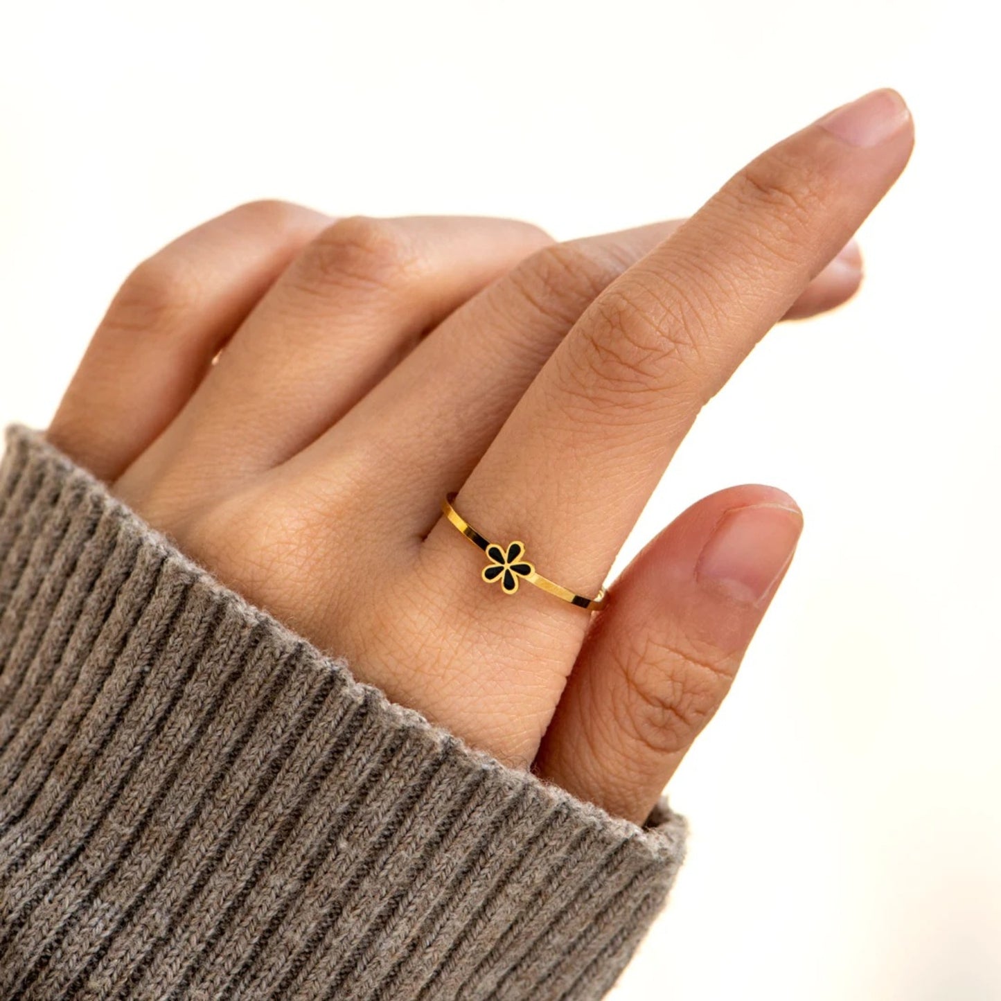 A dainty gold-plated ring with a black flower design on the top part, worn on a person's finger.