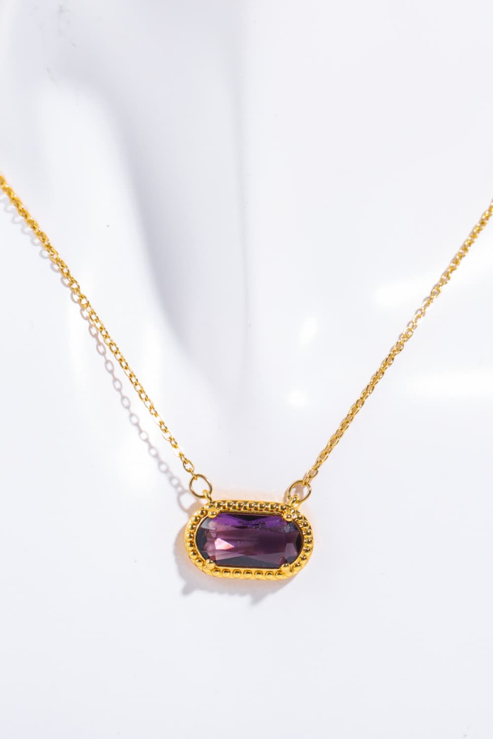 Gold necklace with a purple gemstone on a white background
