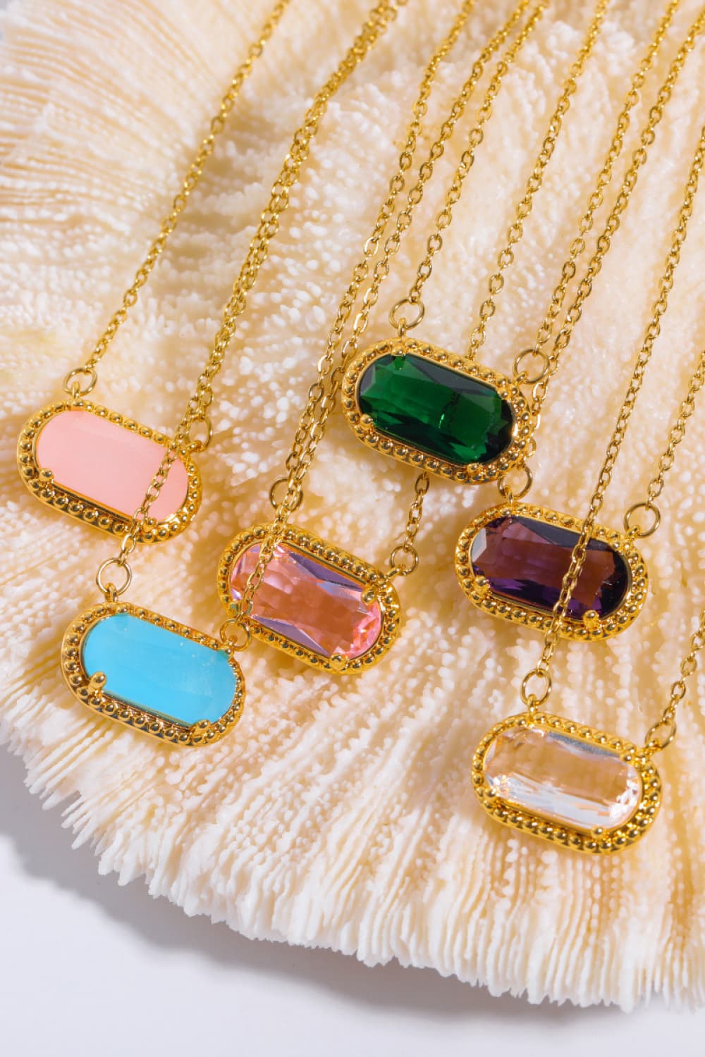 Gold necklaces with colorful pendant stones on a shell background