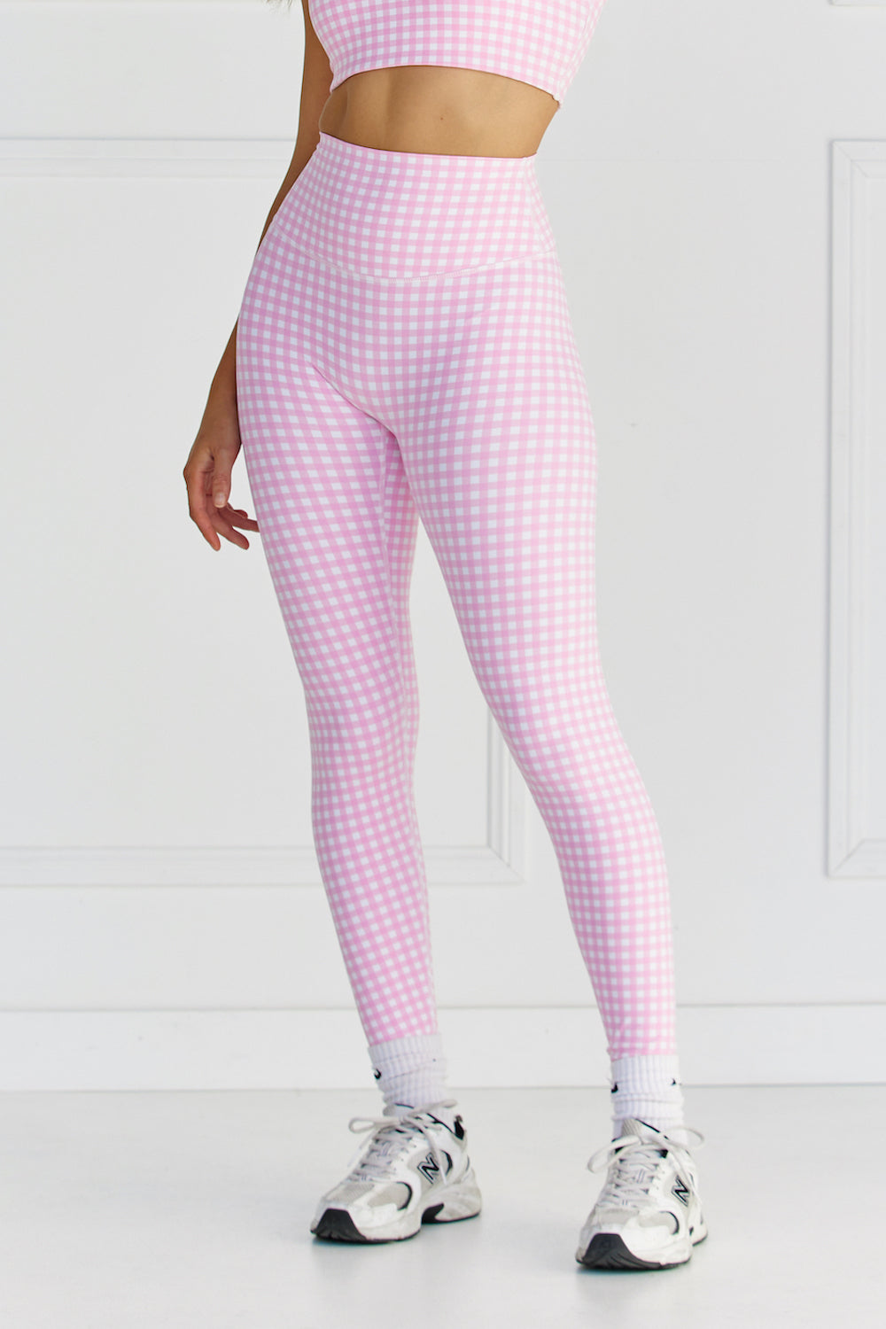 Woman wearing pink & white gingham/checkered leggings and a matching sports bra against a white background