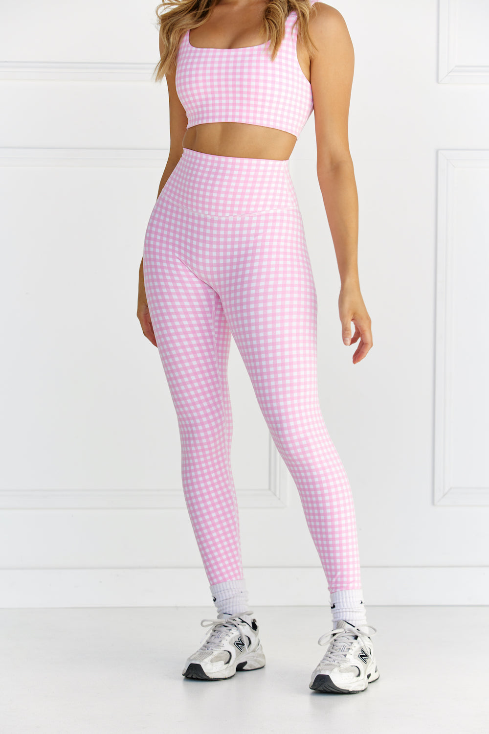 Woman wearing pink & white gingham/checkered leggings and a matching sports bra against a white background