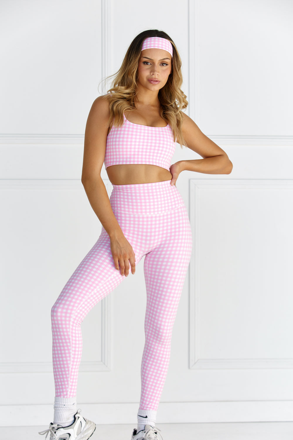 Woman wearing pink & white gingham/checkered leggings and a matching sports bra against a white background