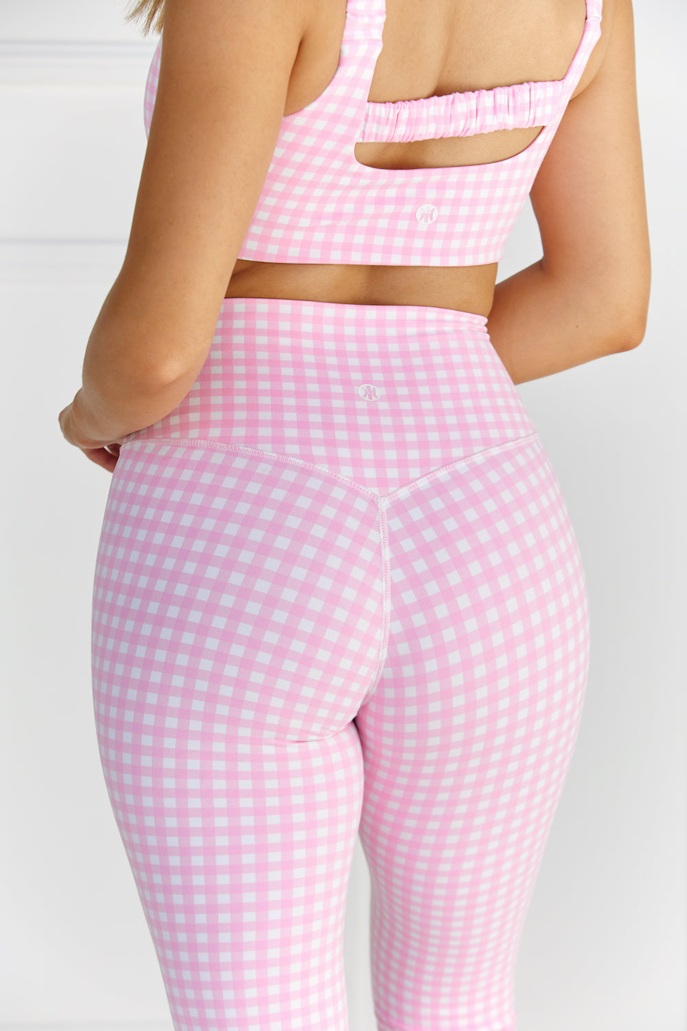 Woman wearing pink & white gingham/checkered leggings and a matching sports bra against a white background