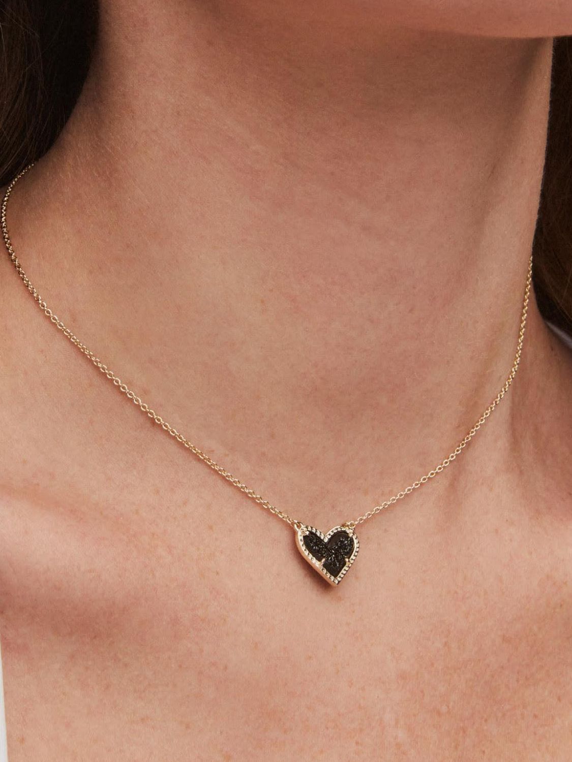 Gold necklace with a black heart-shaped pendant worn by a person