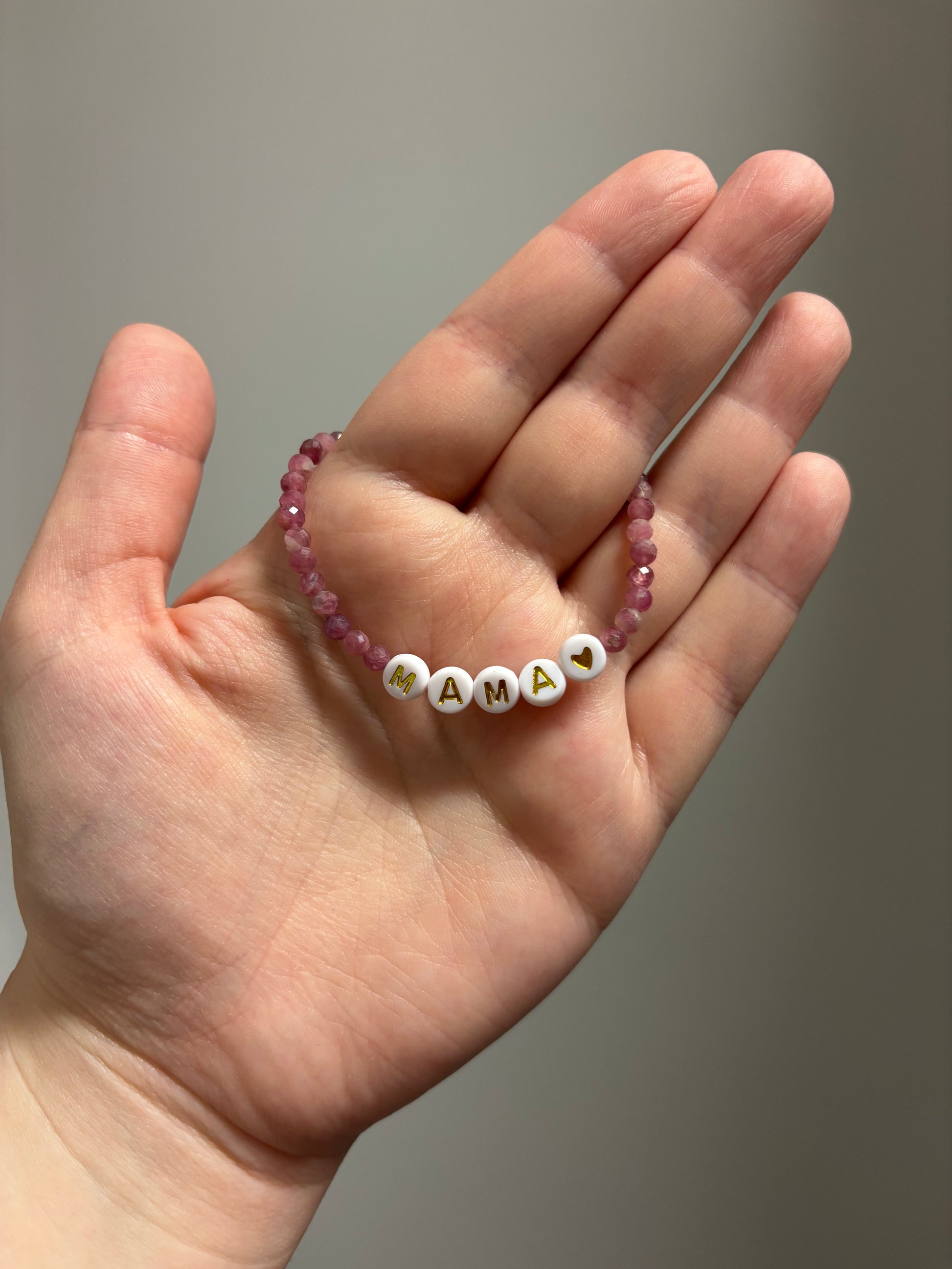 Hand holding a beaded bracelet with 'MAMA' on a plain background