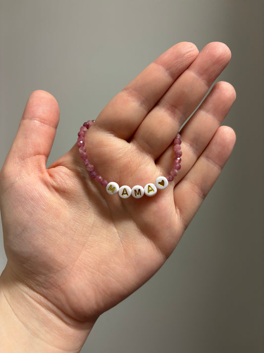 Hand holding a beaded bracelet with 'MAMA' on a plain background