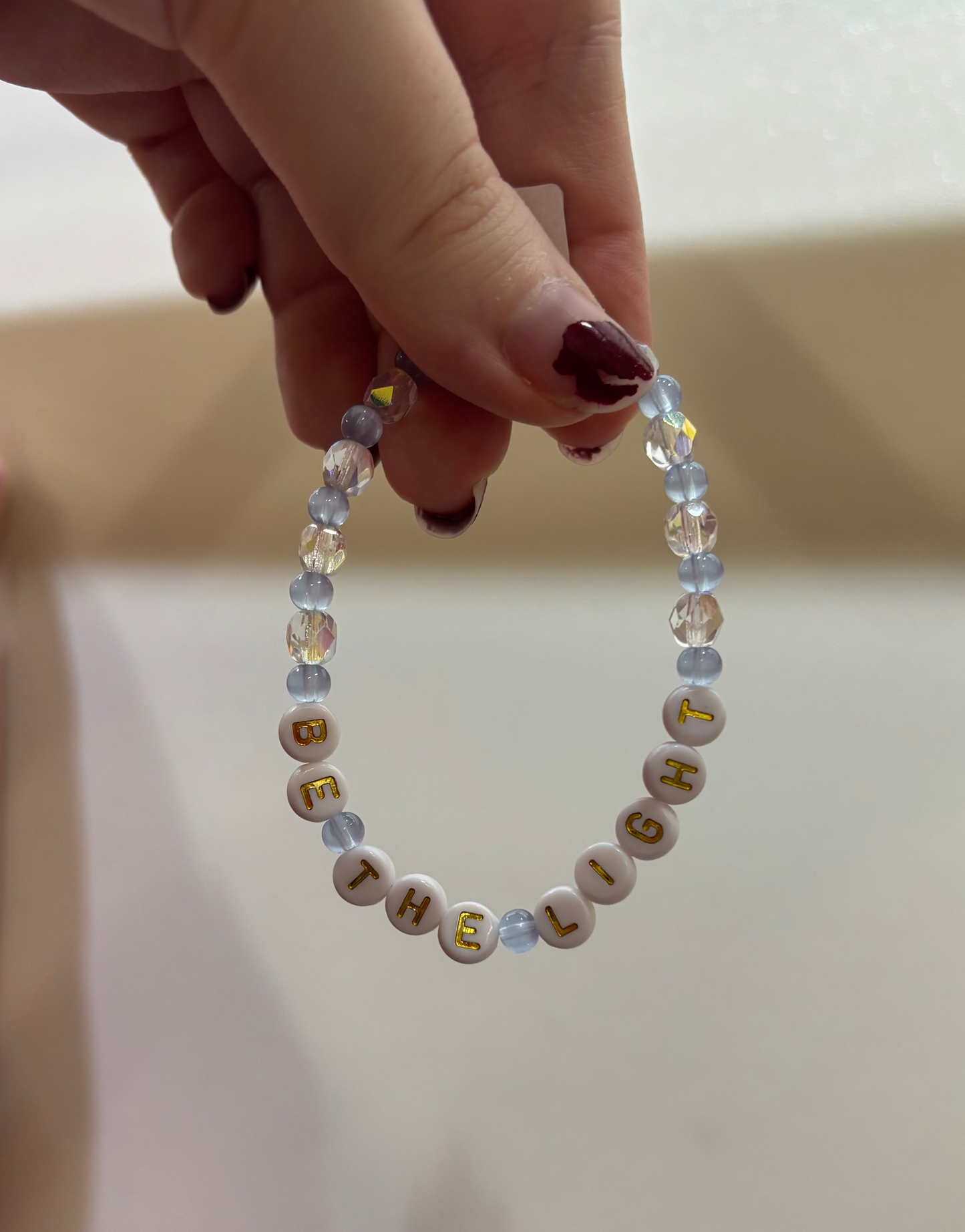 Hand holding a Hanukkah-themed beaded bracelet with letters on a plain background