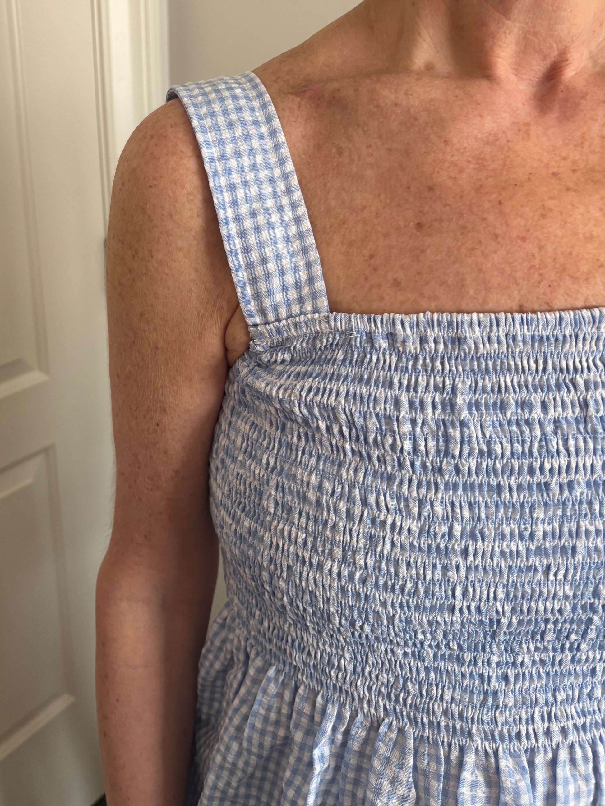 Woman wearing a blue and white gingham checkered top and white denim distressed shorts.
