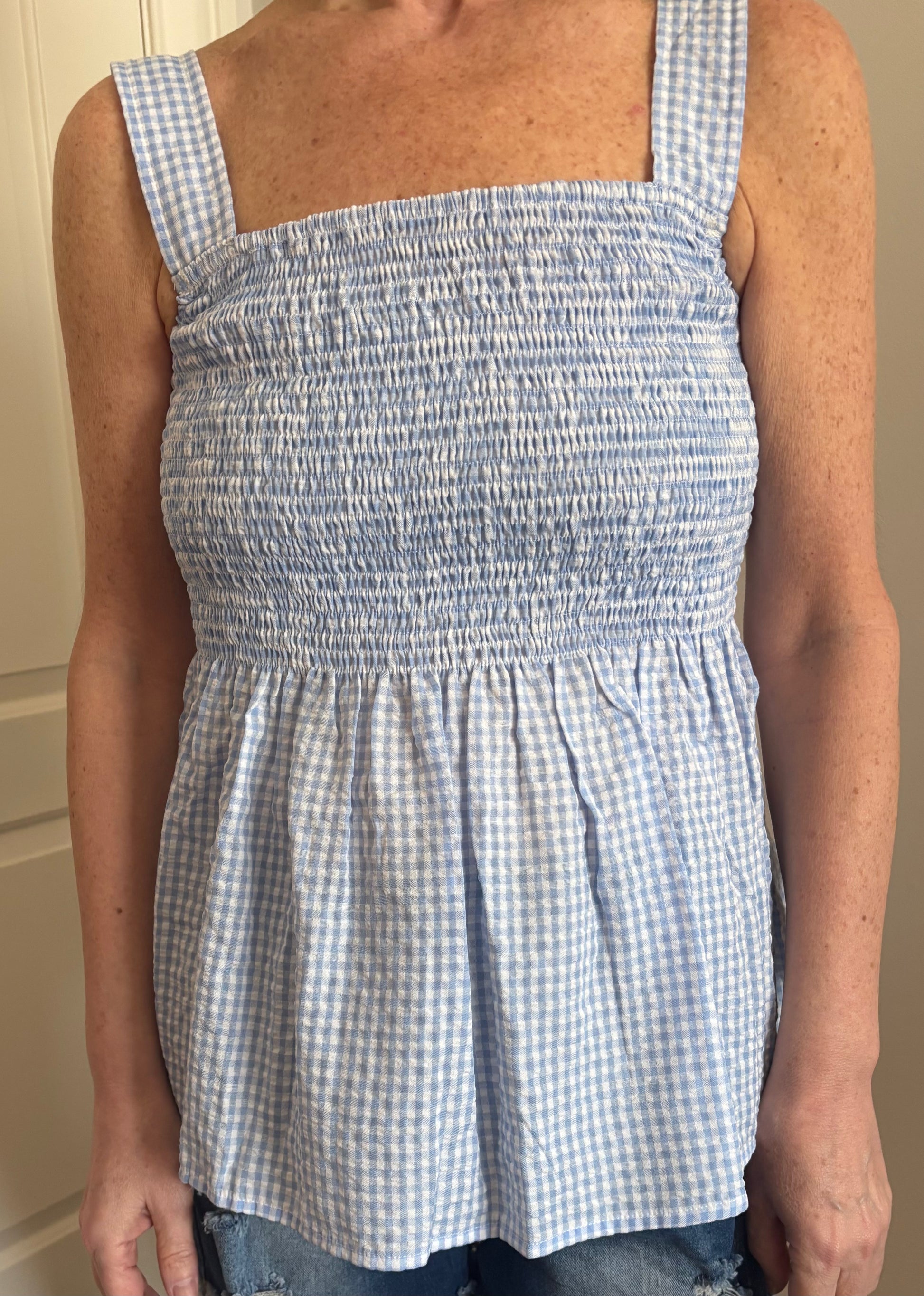 Woman wearing a blue and white gingham checkered top and denim distressed shorts.