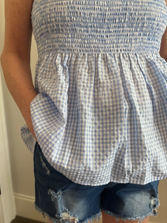 Woman wearing a blue and white checkered top and denim shorts.