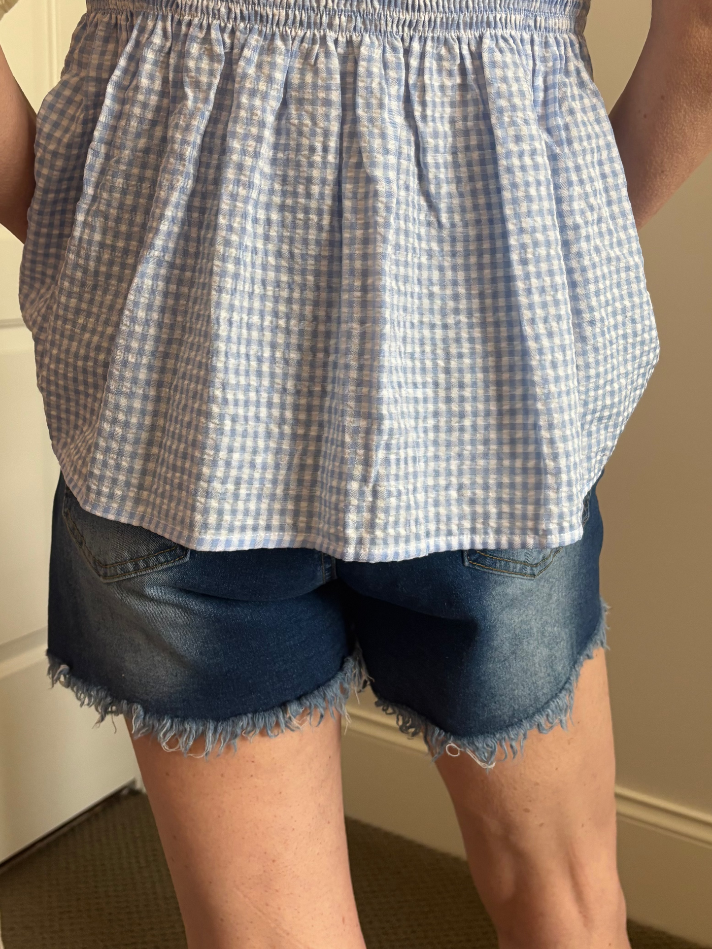 Woman wearing a blue and white checkered top and denim shorts indoors.