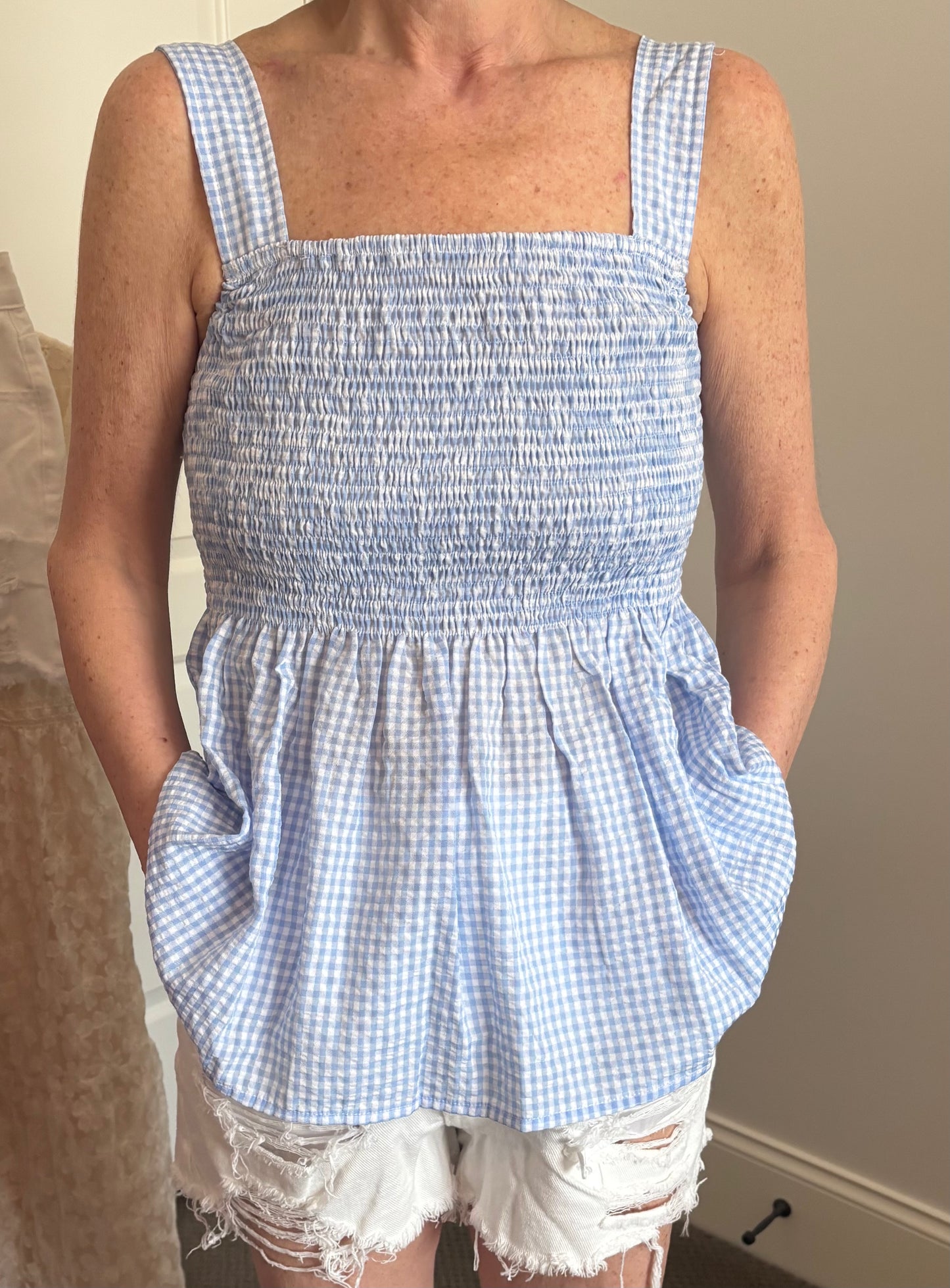 Woman wearing a blue and white gingham checkered top and white denim distressed shorts.