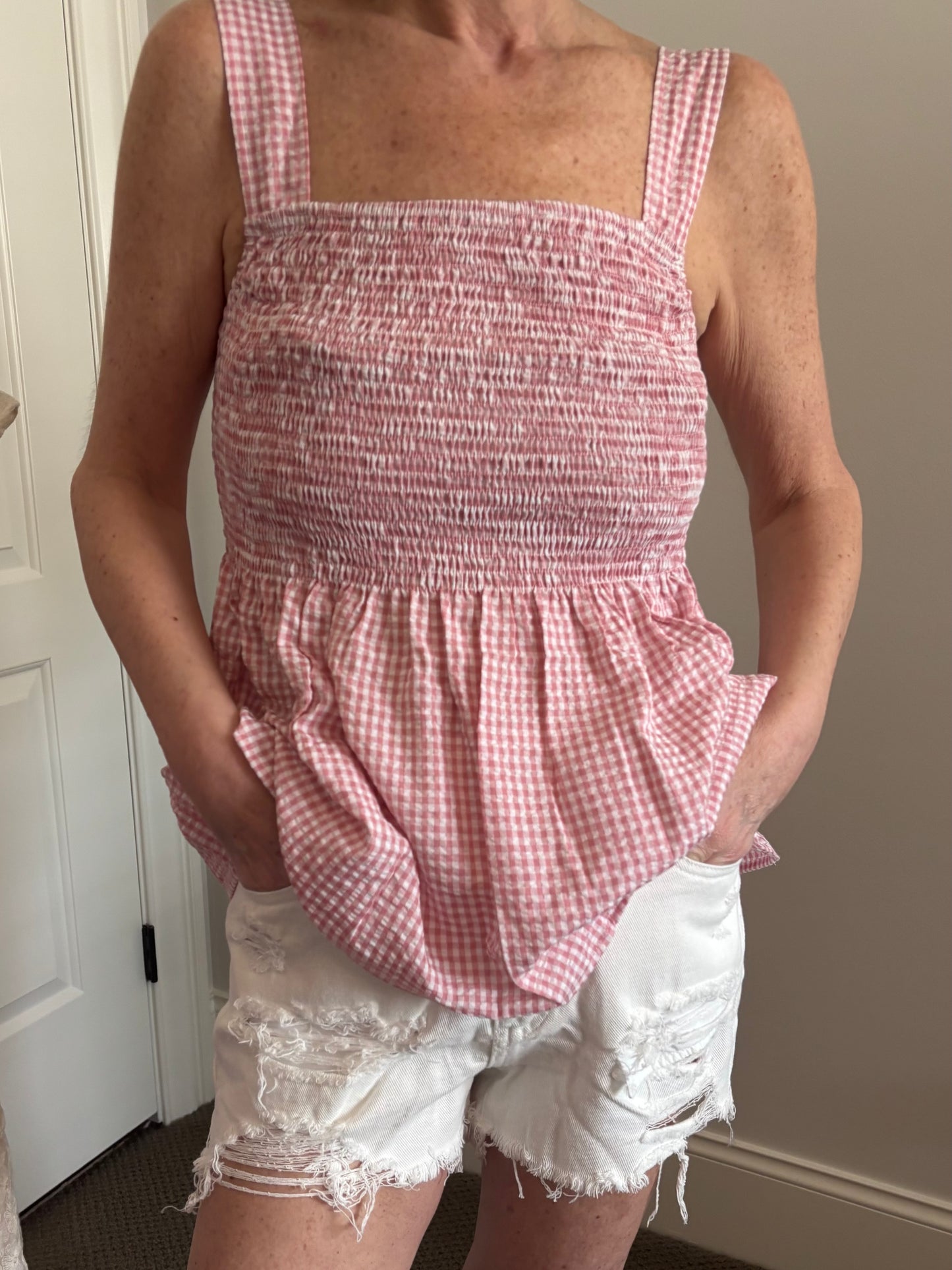 Woman wearing a red and white gingham checkered top and white denim distressed shorts.