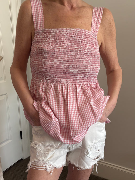 Woman wearing a red and white gingham checkered top and white denim distressed shorts.