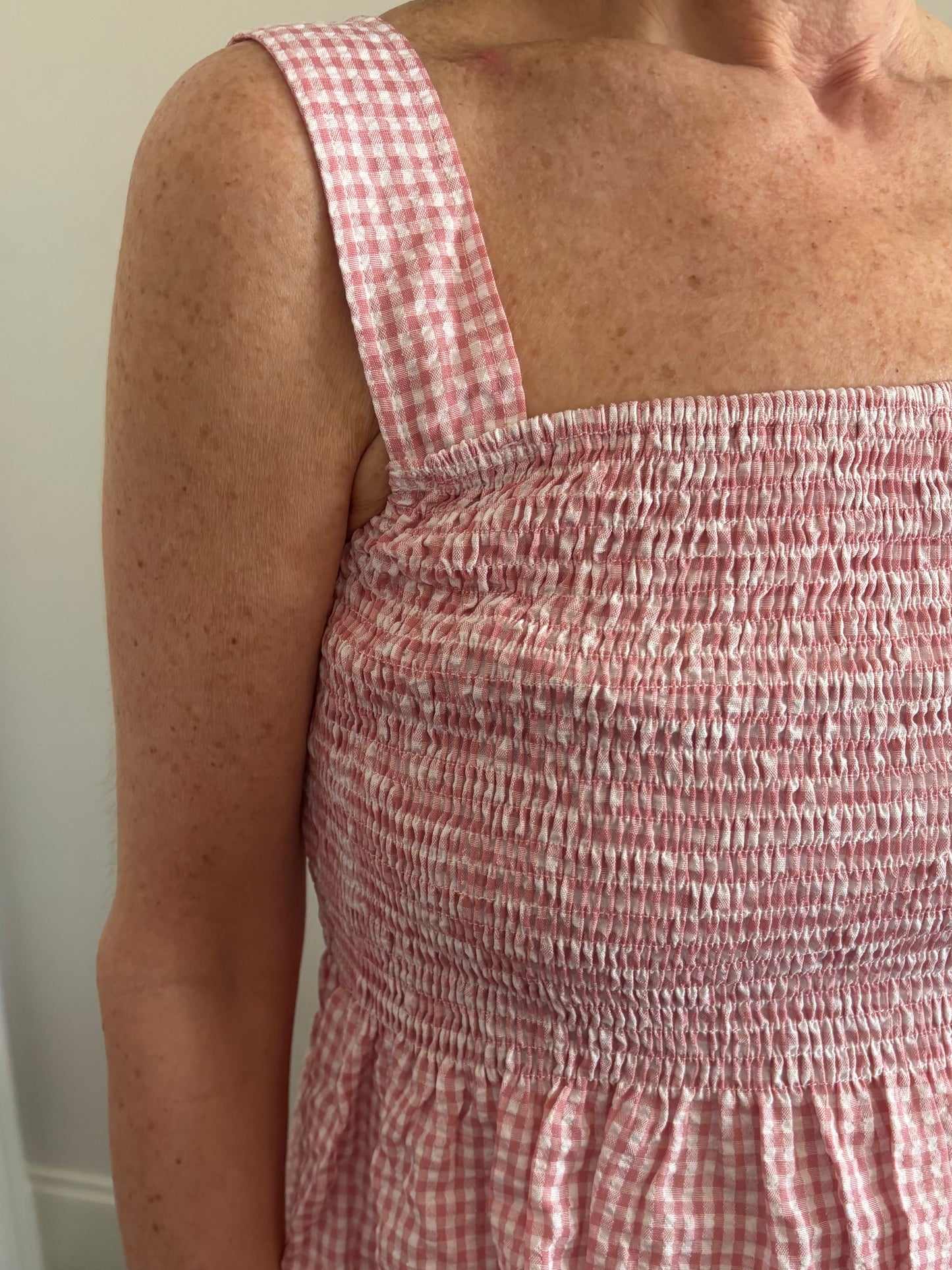Woman wearing a red and white gingham checkered top and white denim distressed shorts.