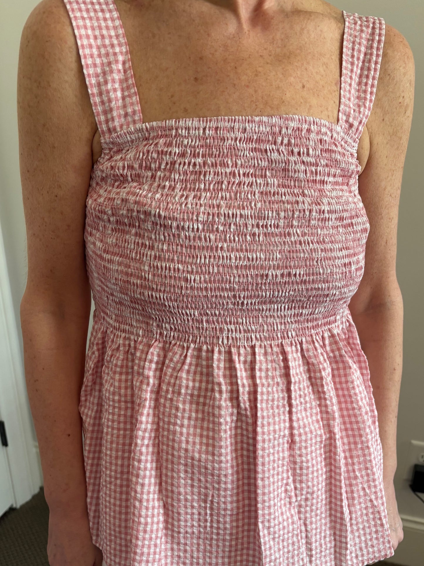 Woman wearing a red and white gingham checkered top and white denim distressed shorts.