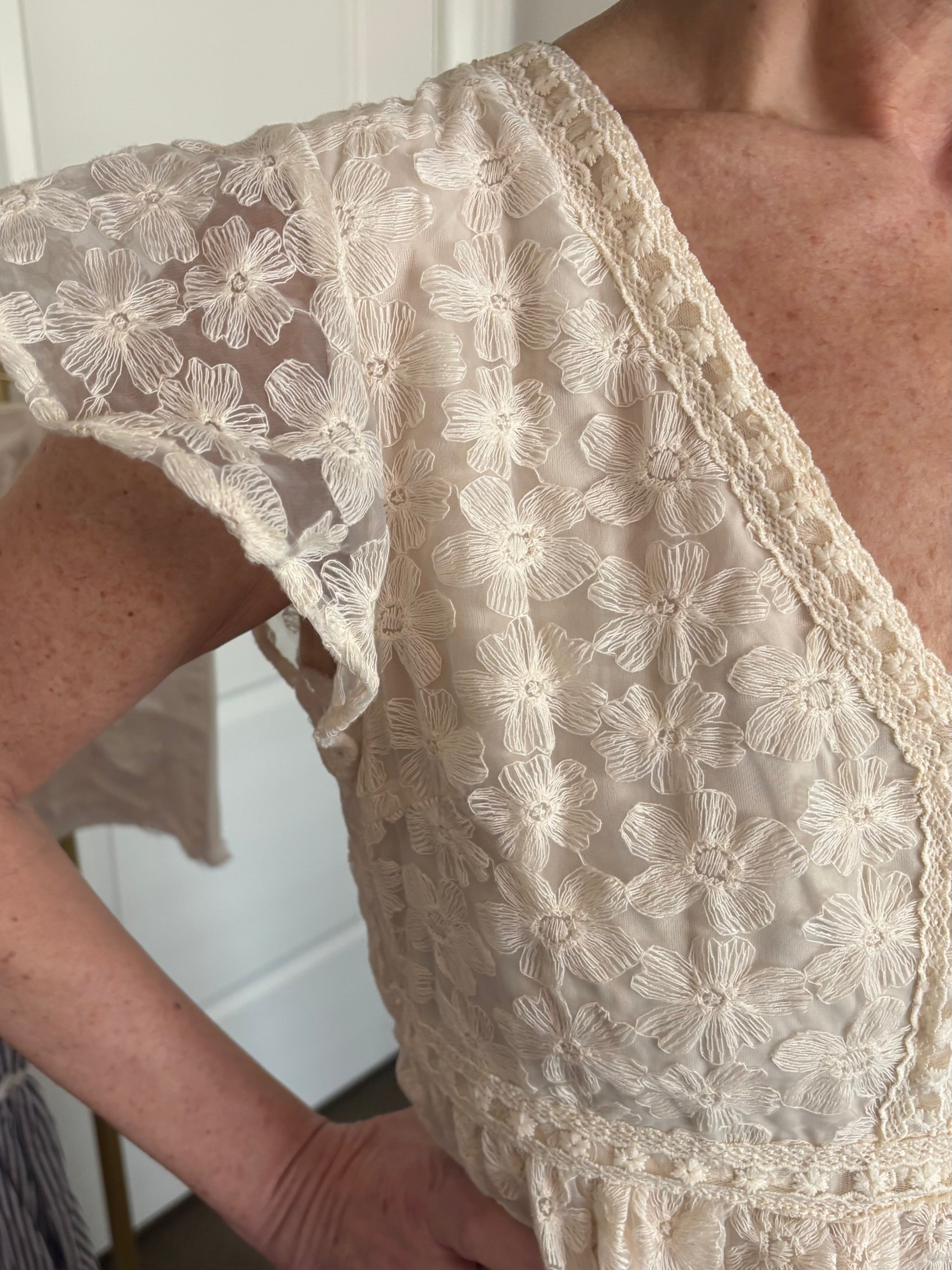 Close-up of a person wearing a beige lace dress with lace floral patterns.
