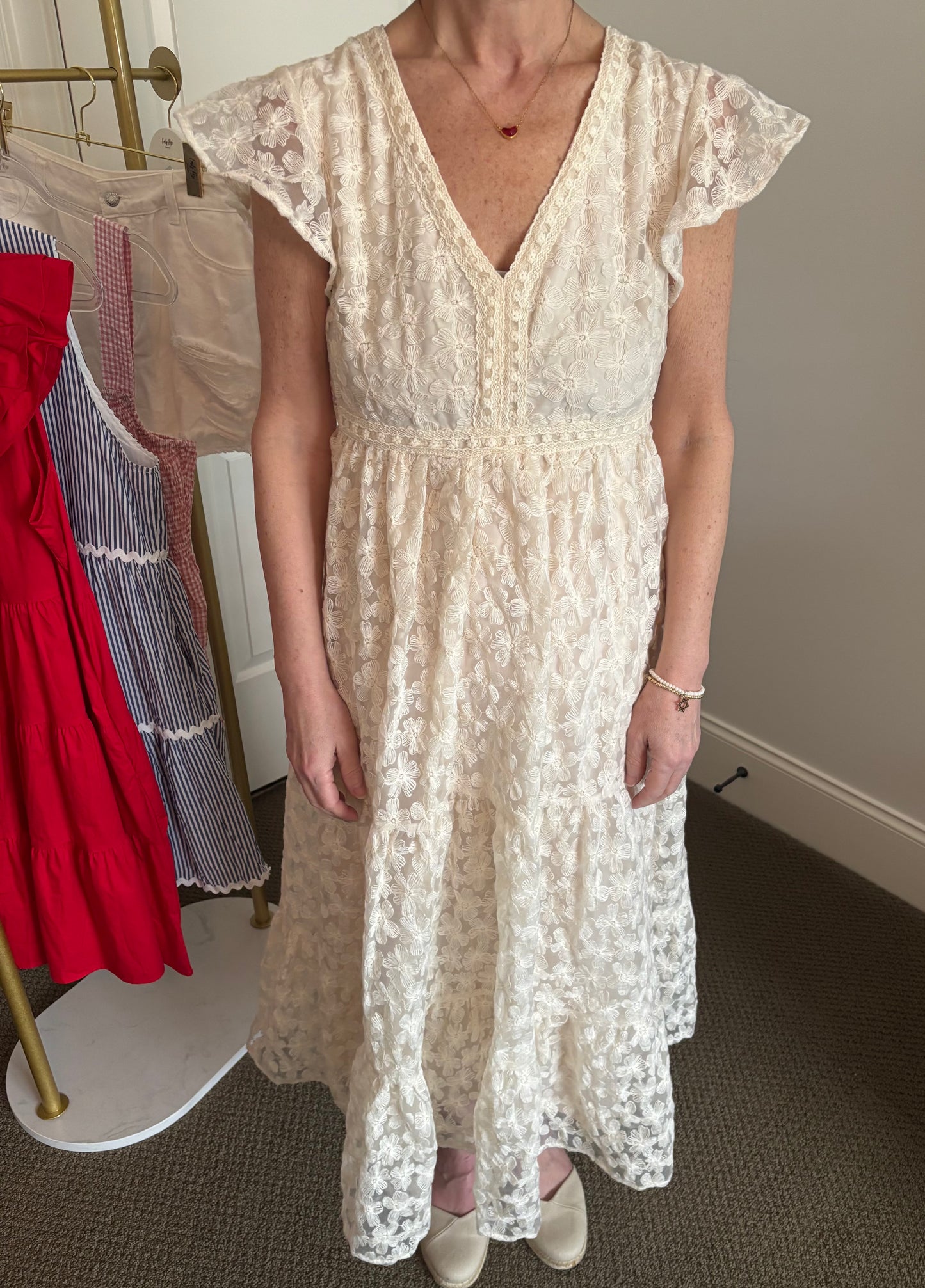 Woman wearing a cream lace dress in a room with a rack of clothes in the background.