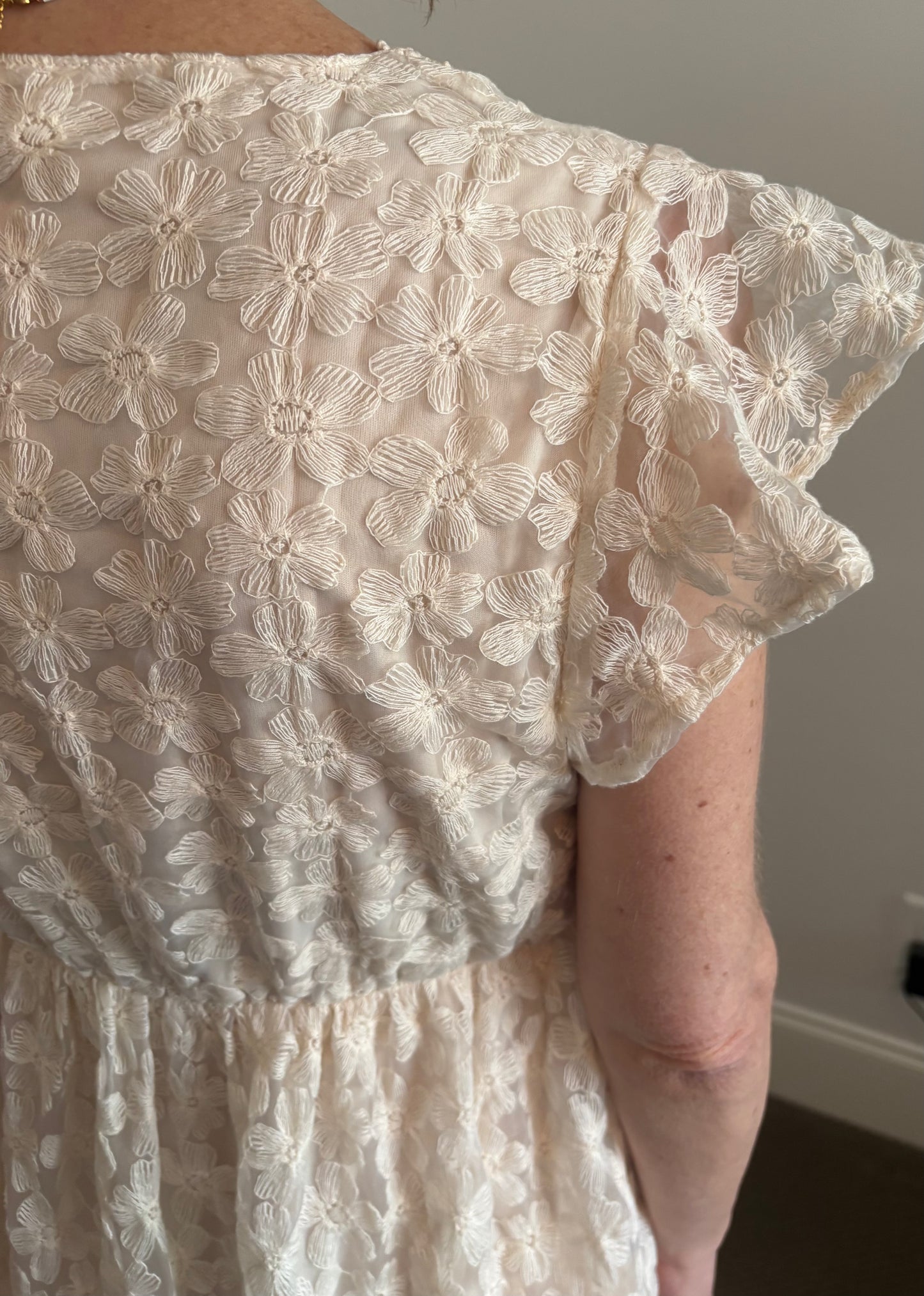 Close-up of a person wearing a white lace dress with floral patterns.