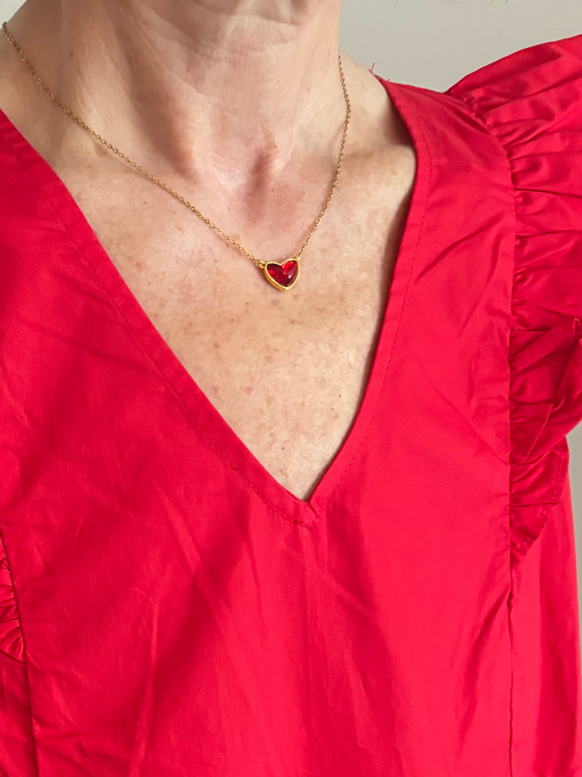 Red dress with a deep red necklace featuring a heart pendant on a neutral background