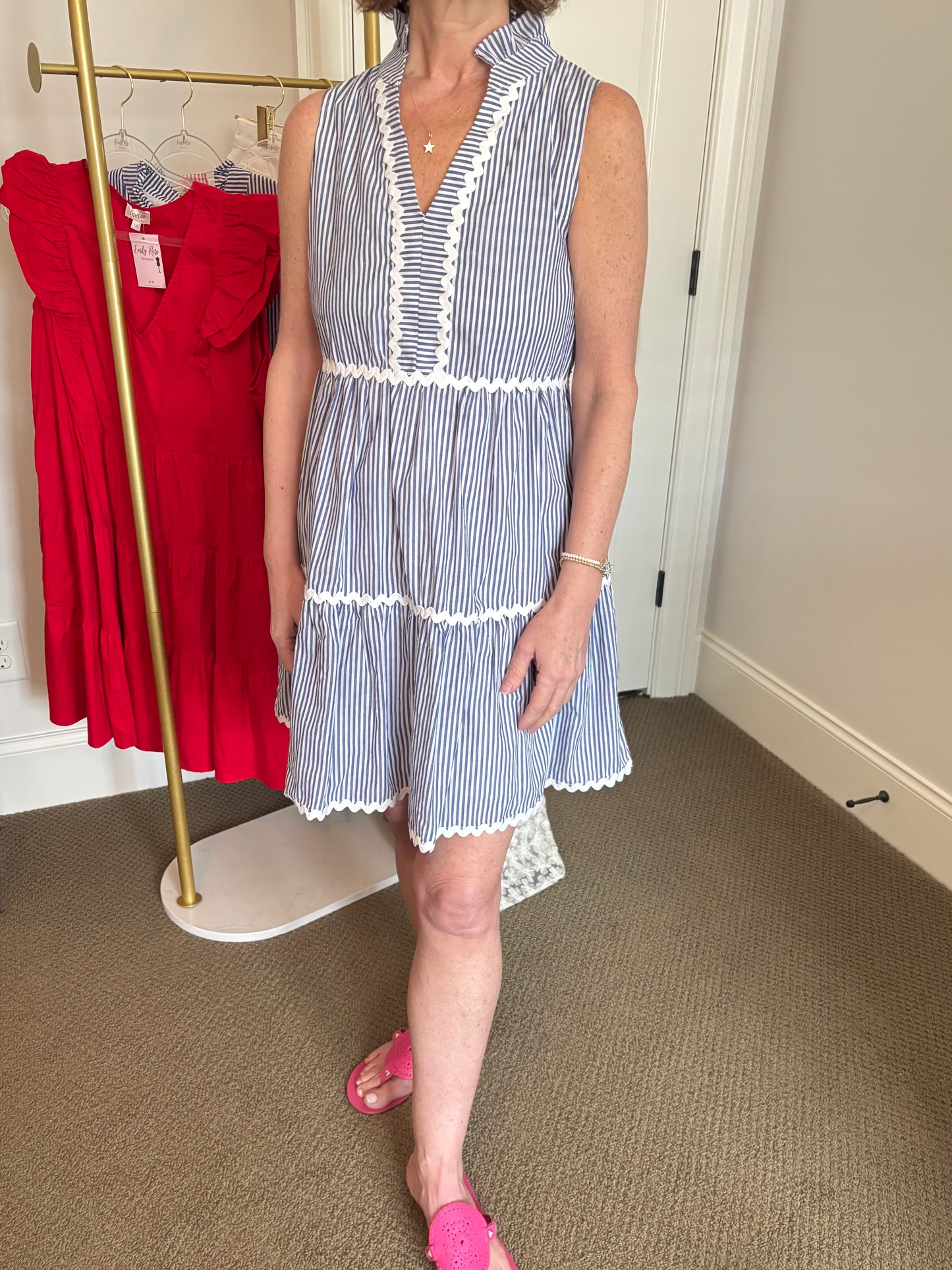 Woman wearing a blue and white striped dress in a room with a red dress on a rack.