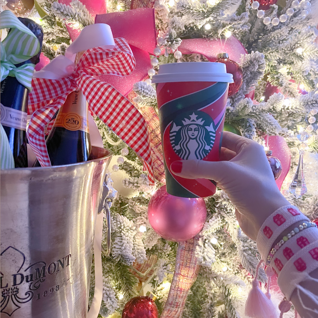 Person holding a red Starbucks cup with adjustable woven Christmas present themed bracelet  in front of a decorated Christmas tree.