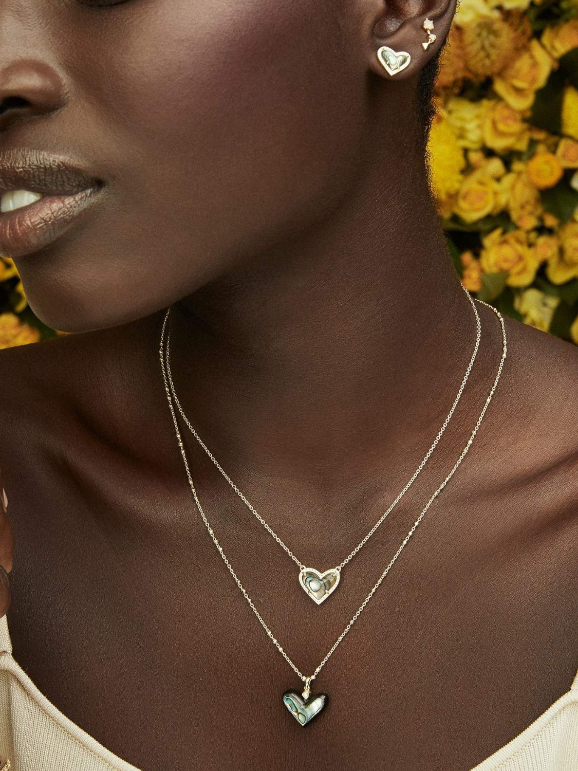 Woman wearing gold necklaces with heart pendants against a floral background