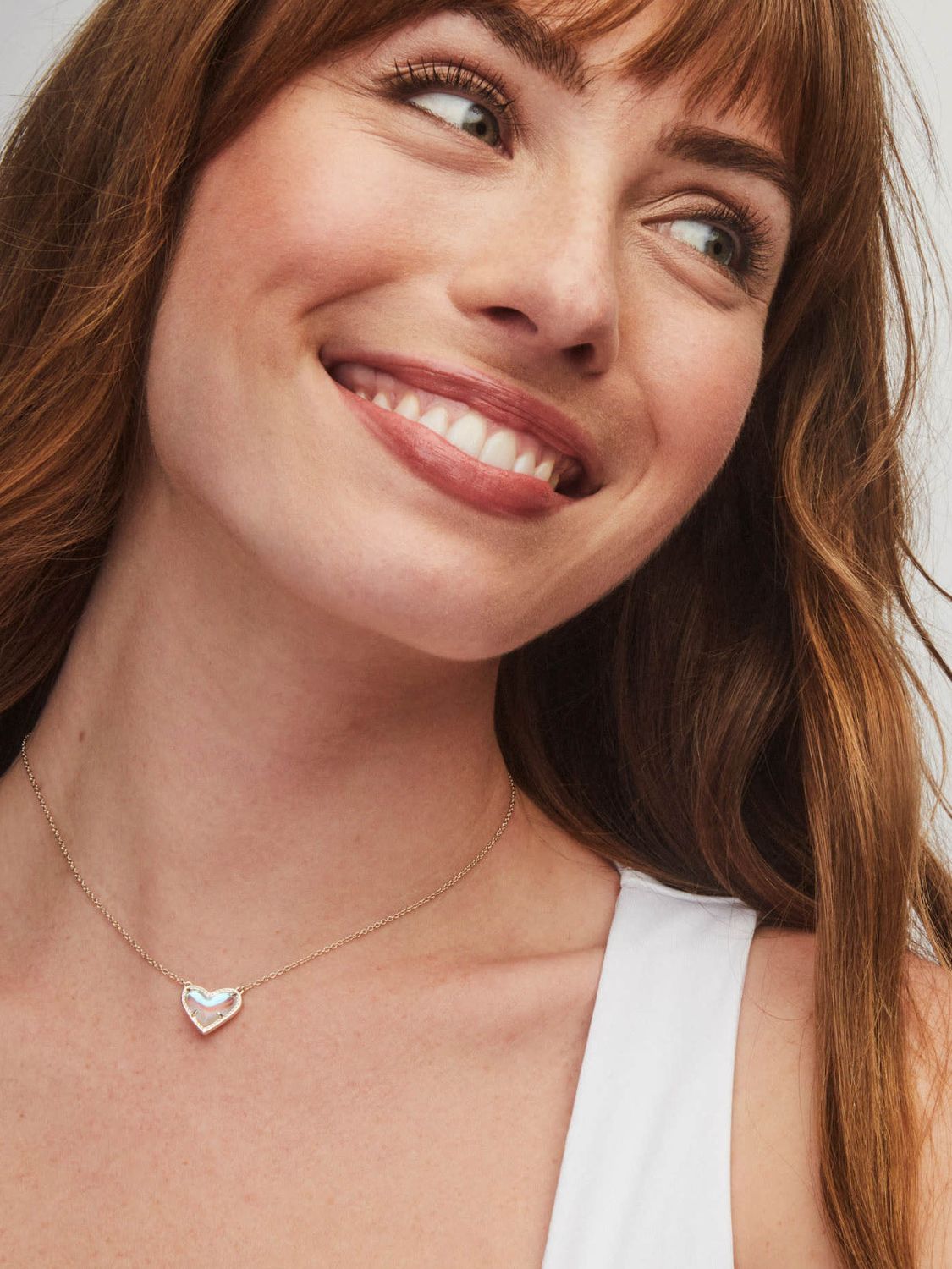 Woman wearing a heart-shaped necklace with a clear gemstone against a neutral background