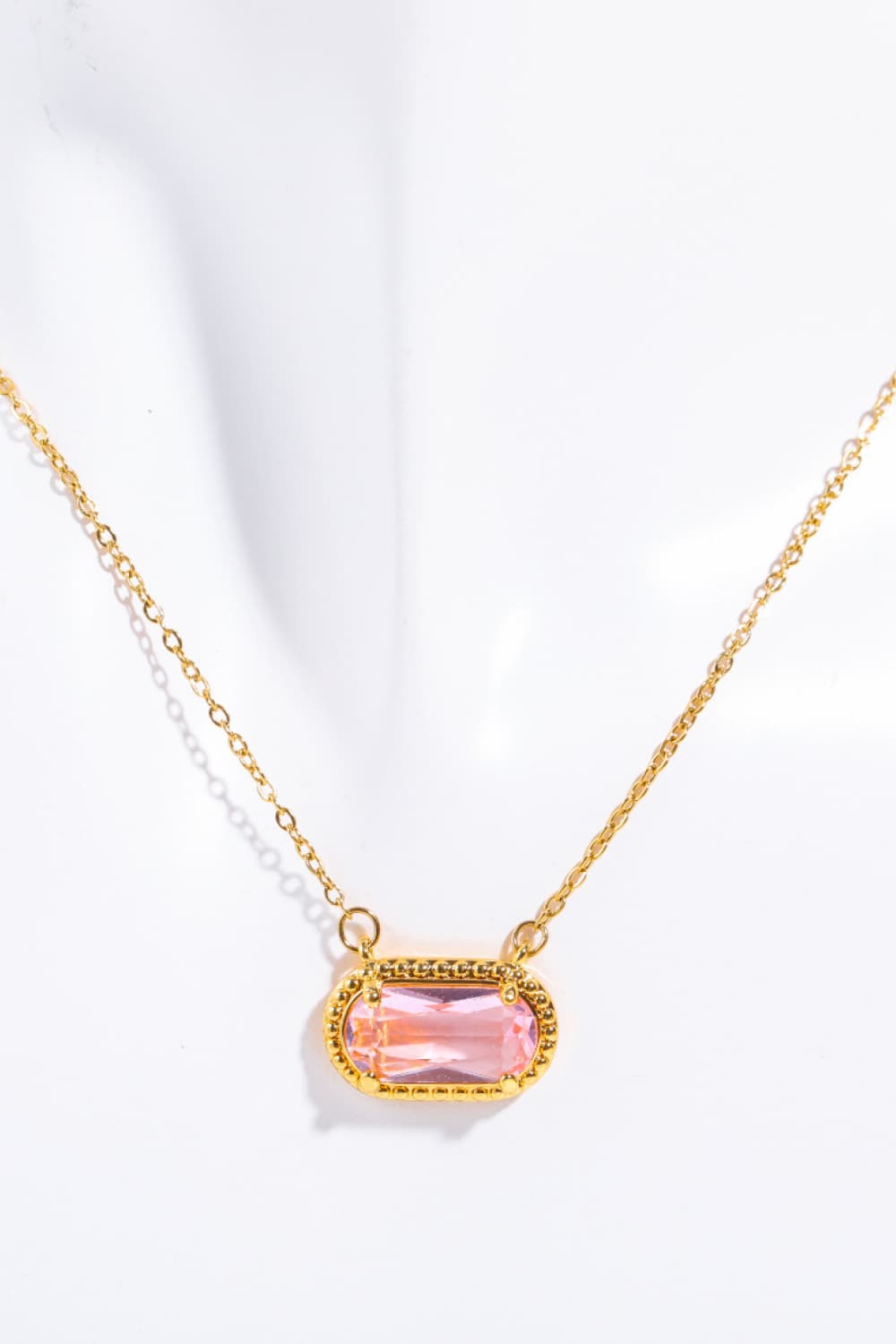 Gold necklace with a pink gemstone pendant on a white background