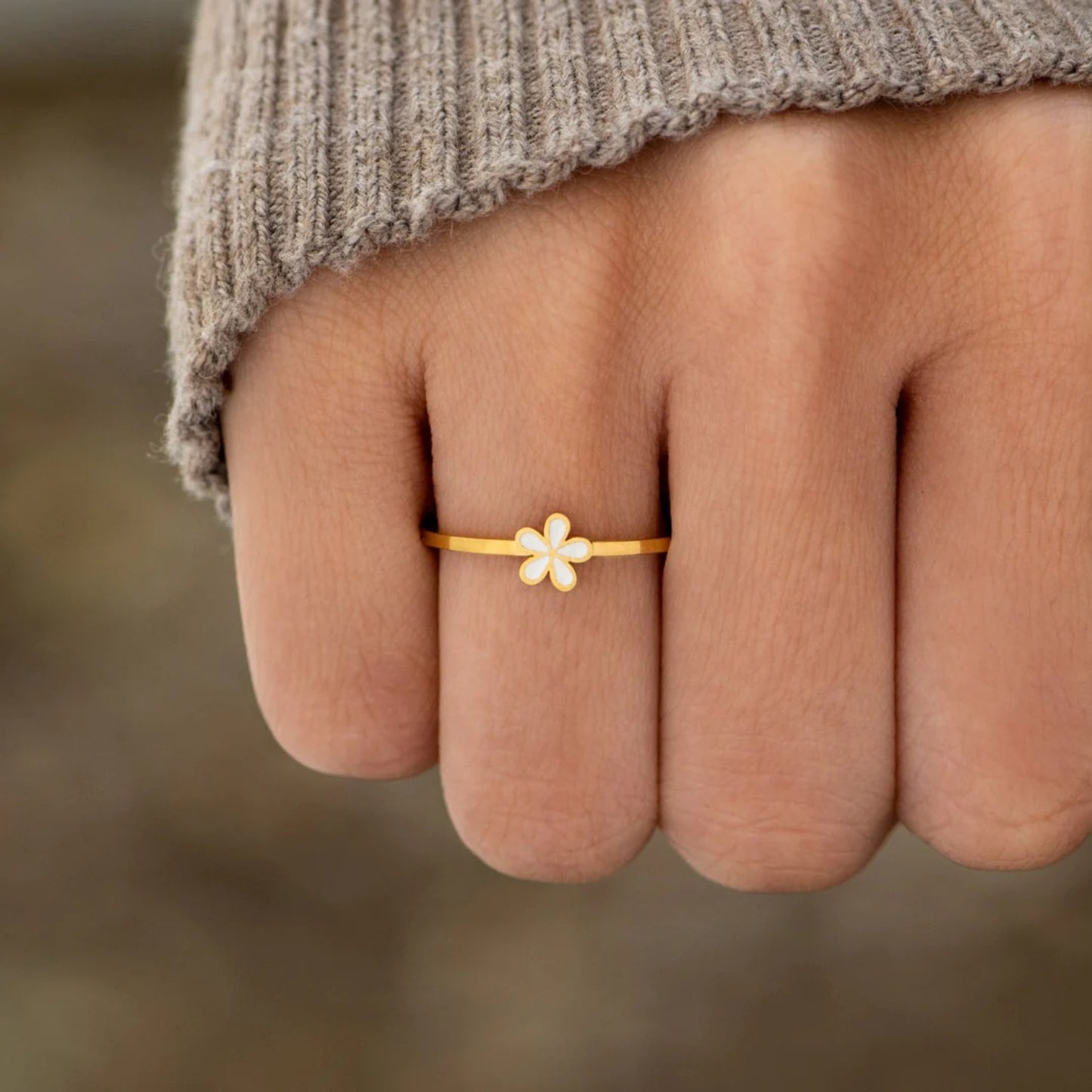 A dainty gold-plated ring with a white flower design on the top part, worn on a person's finger.