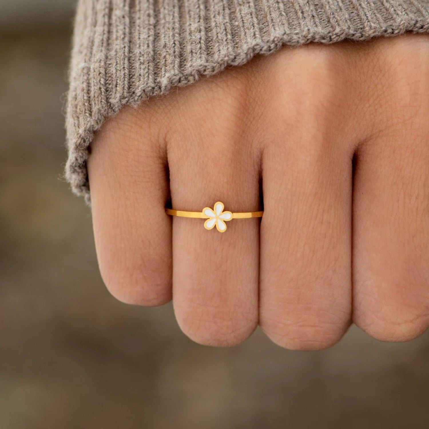 A dainty gold-plated ring with a white flower design on the top part, worn on a person's finger.