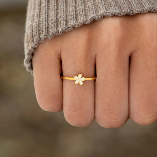 A dainty gold-plated ring with a white flower design on the top part, worn on a person's finger.