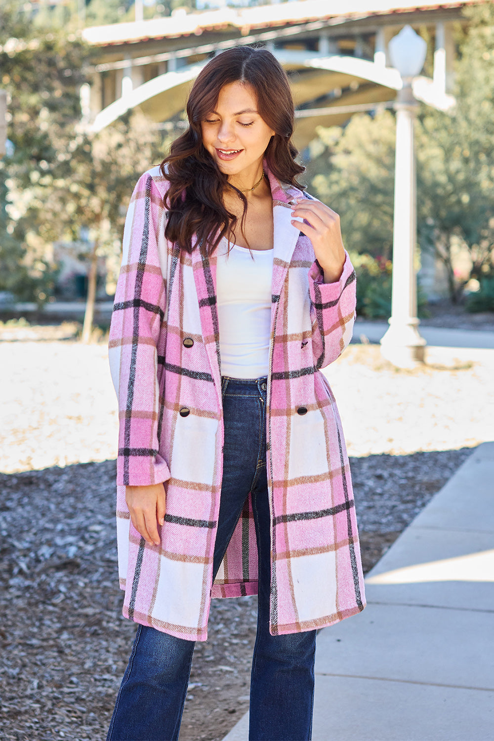 A woman wearing a pink plaid button-up coat with long sleeves and a V-neckline, paired with a white top and blue jeans.