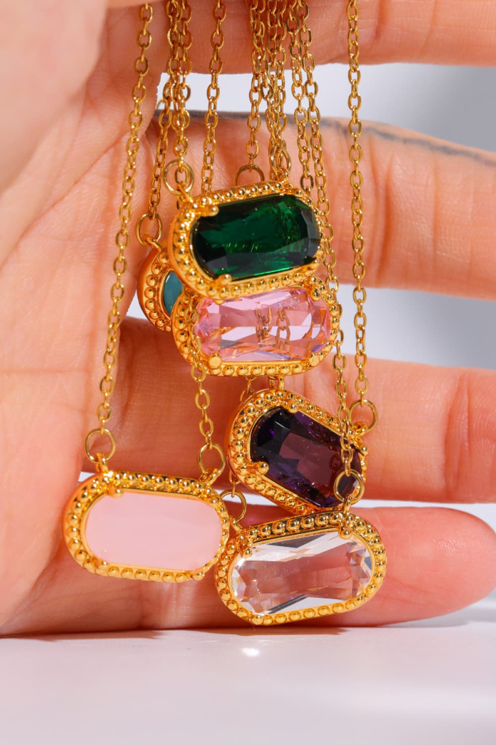 Gold necklace with colorful gemstones held in a hand against a neutral background