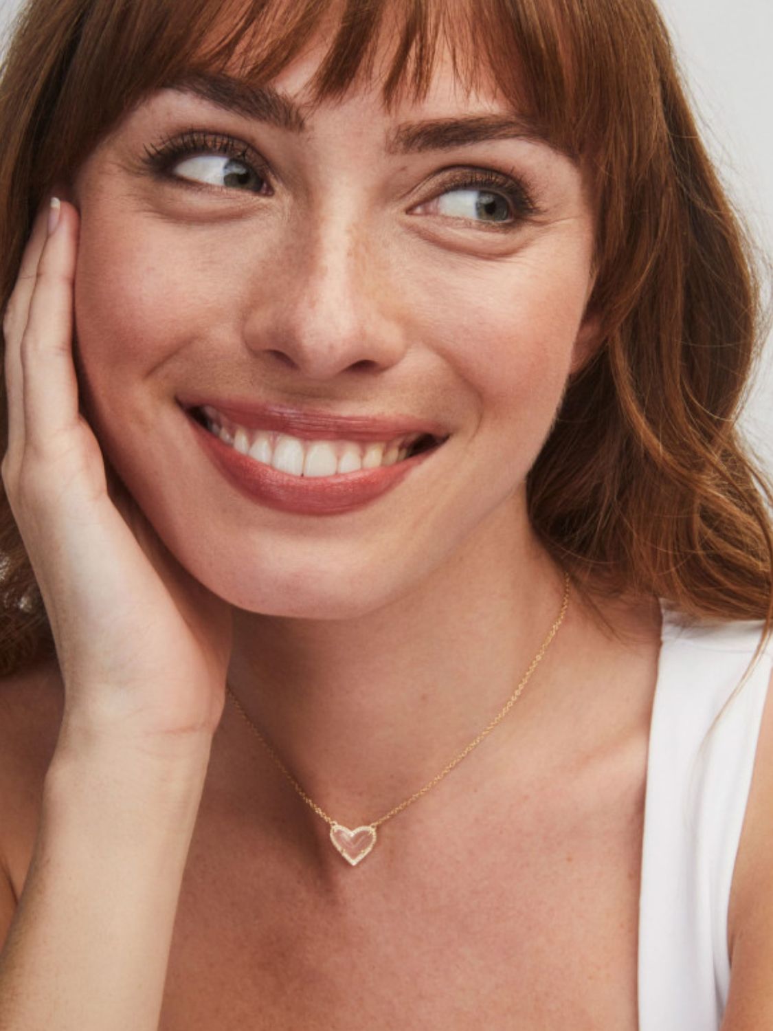 Woman wearing a gold heart-shaped necklace against a neutral background
